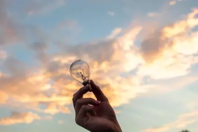 A hand holding a lightbulb against a bright sky