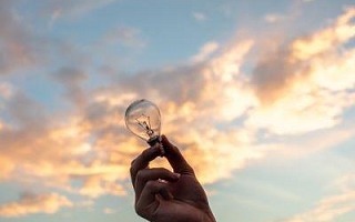 Someone holding a lighbulb with the sky in the background